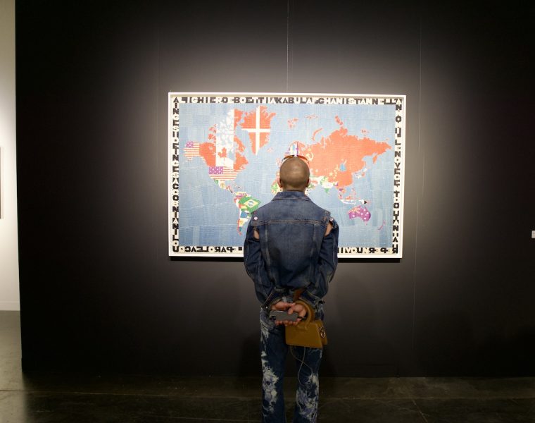 Tariffs and the global art market at Miami Art Week. Visitor views international artwork highlighting cross-border exchange at an art fair.